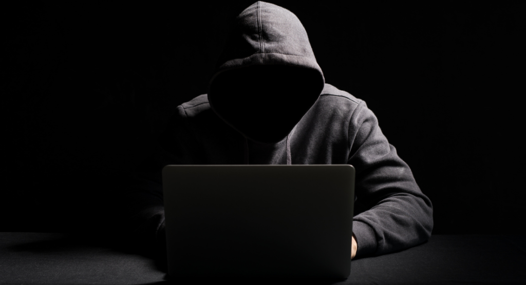 A computer hacker in a black hoodie in a dark room. Crime insurance can help protect your business's cryptocurrency investments from hackers and other crimes.