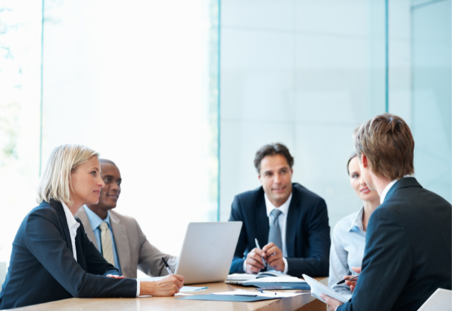 five professionals sitting at a table having a business meeting