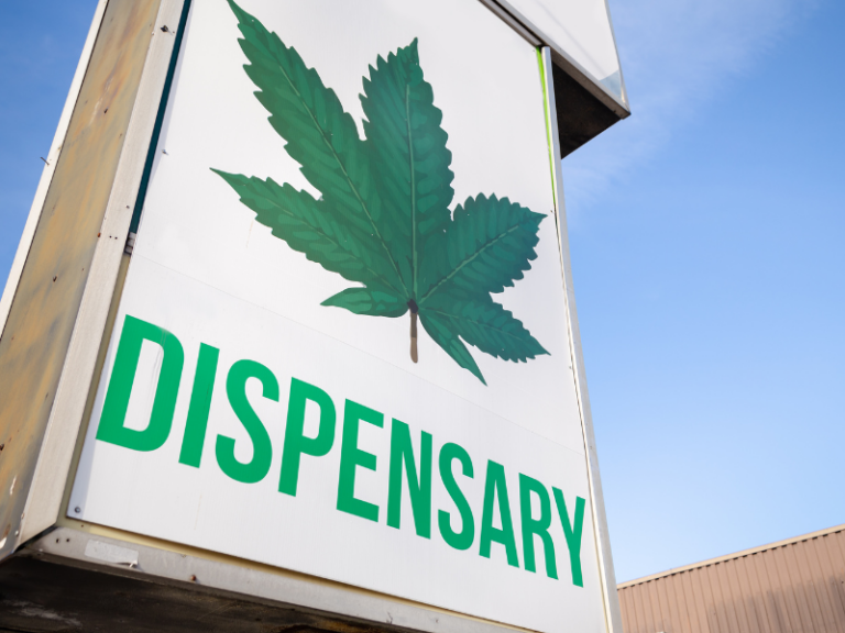 An outdoor shop sign that says "dispensary" and has a green cannabis leaf illustration above it. This is an example of a business that requires cannabis dispensary insurance!