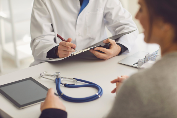 A doctor writing on a clipboard while speaking to a patient